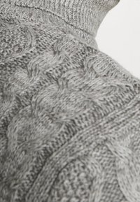 Pull gris en tricot présentant un motif torsadé texturé avec un col montant et des détails côtelés. Matière douce avec un aspect épais.