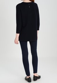 Marinblå tunika med texturerat tyg, rund halsringning, trekvartslånga ärmar och knäppning bak. Matchas med mörka skinny jeans och lägenheter.