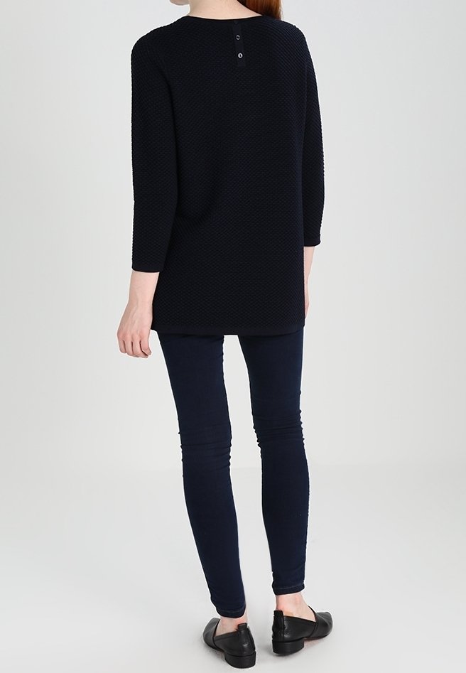 Marinblå tunika med texturerat tyg, rund halsringning, trekvartslånga ärmar och knäppning bak. Matchas med mörka skinny jeans och lägenheter.