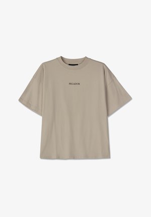 Beežist puuvillast T-särk, üle mõõdu suurusega, lühikeste varrukatega, ümmarguse kaelusega ja keskel must tekst "PEGADOR". Ilma mustrite või lisadeta.