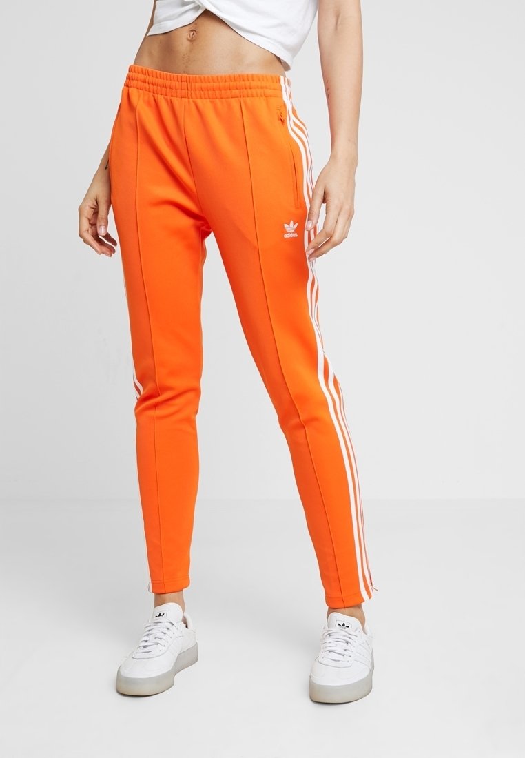 Orange idrottsbyxor med vita sidostråk, elastisk midja och smal passform. Tillverkade av ett mjukt tyg, med en broderad logotyp.