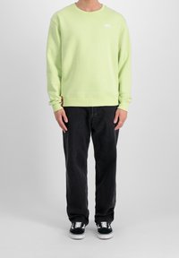 Lime green sweatshirt with ribbed cuffs and hem, featuring a small white logo. Paired with black loose-fit pants and black sneakers.