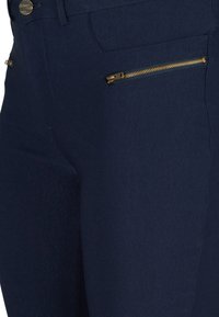 Marineblauwe broek van soepel stof met metallic gouden ritszakken en een slank ontwerp dat de op maat gemaakte pasvorm benadrukt.