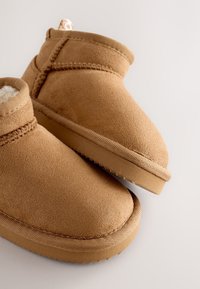 Stivaletti alla caviglia in pelle scamosciata color cuoio con morbido rivestimento interno, punta tonda e suola esterna strutturata. Presentano un design cucito e un'ascella per indossarli facilmente.