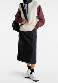 Hooded cream and burgundy sweatshirt with long sleeves, paired with a black midi skirt featuring pockets, and white sneakers with accents.
