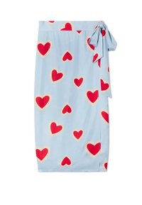 Φούστα τύπου wrap ανοιχτού γαλάζιου χρώματος με κόκκινες καρδιές που περιβάλλονται από σχέδιο δαντέλας σε κρεμ απόχρωση και φιόγκο δεξιά στη μέση.