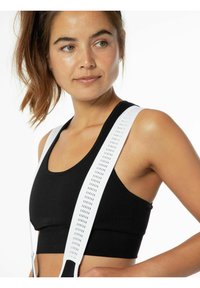 Top corto a costine nero con spalline regolabili bianche e dettagli perforati, inquadrato sulla parte superiore del corpo di un modello con uno sfondo neutro.