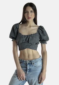 Sort-hvid ternet crop top med pufærmer, flæsefront og tætsiddende design, kombineret med høj talje lyseblå jeans.