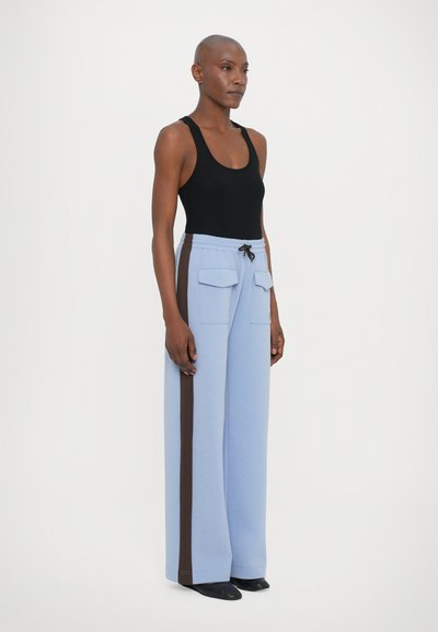 Calças largas de tom azul claro com uma faixa lateral castanha, apresentando dois bolsos frontais e uma cintura com cordão. Combinadas com uma blusa de alças preta.