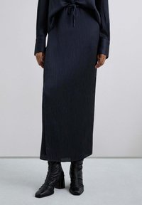 Larga falda de canalé azul marino hecha de una suave tela, con cintura con cordón, combinada con botas de tobillo negras texturizadas.