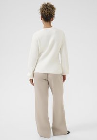 Pulover alb, texturat, cu mâneci lungi, purtat cu pantaloni bej, cu croială largă. Designul este simplu, având un gât rotund și accente canelate.