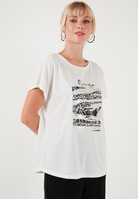 Hvid t-shirt med korte ærmer, der har et sort og beige grafisk design. Glat tekstur med en rund halsudskæring og en afslappet pasform.