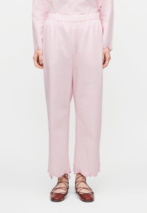 Osoba nosząca luźne, jasnoróżowe spodnie z falistym obszyciem i detalami z oczkami, w połączeniu z brązowymi płaskimi butami na sznurowadła.