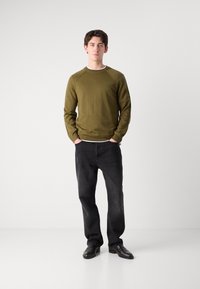 Olijfgroen gebreid sweatshirt met een ronde hals, textuurpatroon, gecombineerd met zwarte rechte jeans en zwarte schoenen.