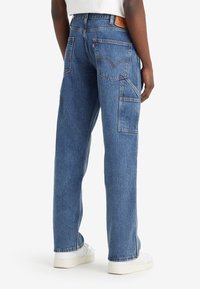 Blå denimjeans med avslappnad passform, flera fickor och en signaturdesign för bakfickan. Har hög midja och ljus tvättstruktur.