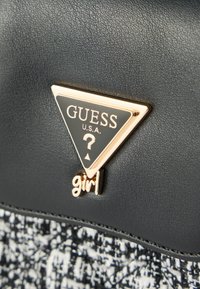 Sac à main en cuir noir avec panneau en tissu texturé, doté d'une plaque logo triangulaire dorée et d'un accent "girl" en écriture cursive.