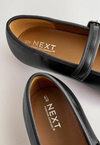 Melnas ādas baleta kurpes ar siksniņu, ar gludu tekstūru, brūnu iekšzoli un ar uzrakstu "NEXT FOREVER COMFORT" iekšpusē.
