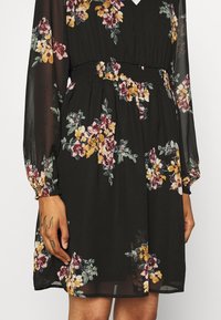 Černé květinové šaty s dlouhými průhlednými rukávy, nařaseným pasem a vícebarevnými květinami v růžové, žluté a zelené barvě. Hladká textura, do kolen.