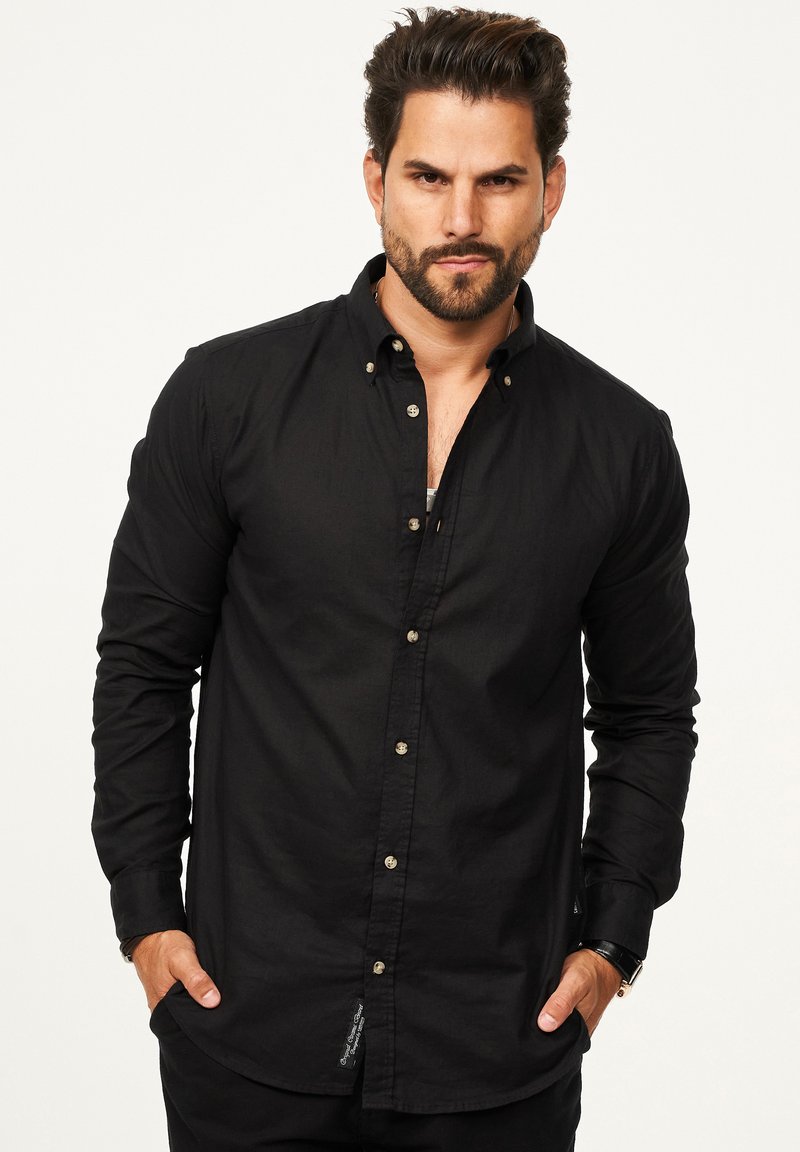 Schwarzes Langarmhemd mit Button-Down-Kragen, das ein tailliertes Design, eine glatte Textur und subtile Nähte aufweist. Knöpfe in kontrastierender Farbe.