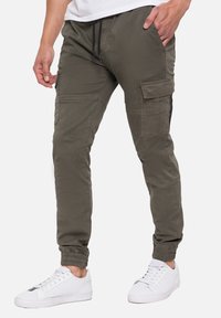 Olijfgroene cargo broek, met meerdere zakken, een slim fit, elastische boorden en een trektouw in de taille, gecombineerd met witte sneakers.