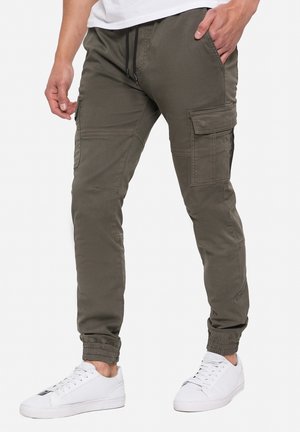 Pantalons cargo vert olive, dotés de plusieurs poches, d'une coupe slim, de poignets élastiques et d'une taille à cordon, associés à des baskets blanches.