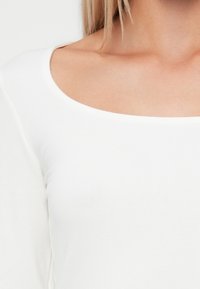 Witte lange mouwen shirt met een brede, ronde halslijn. Soepele katoenen stof met een lichte rek en een aansluitend ontwerp rond de schouders.
