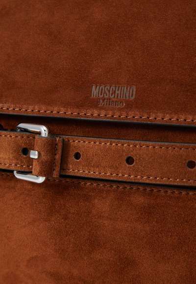 Geantă din suede maro cu o cataramă metalică argintie, având un accent cusut și un logo embossat "MOSCHINO Milano." Textură netedă.