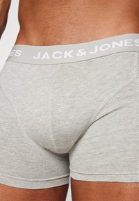 Boxeri din bumbac gri, cu o textură moale, având un tiv elastic alb inscripționat cu "JACK & JONES." Vedere de aproape a țesăturii.