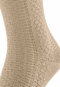 Calzino beige caratterizzato da un motivo tessuto testurizzato con linee diagonali e piccoli diamanti, realizzato in un materiale morbido ed elastico.