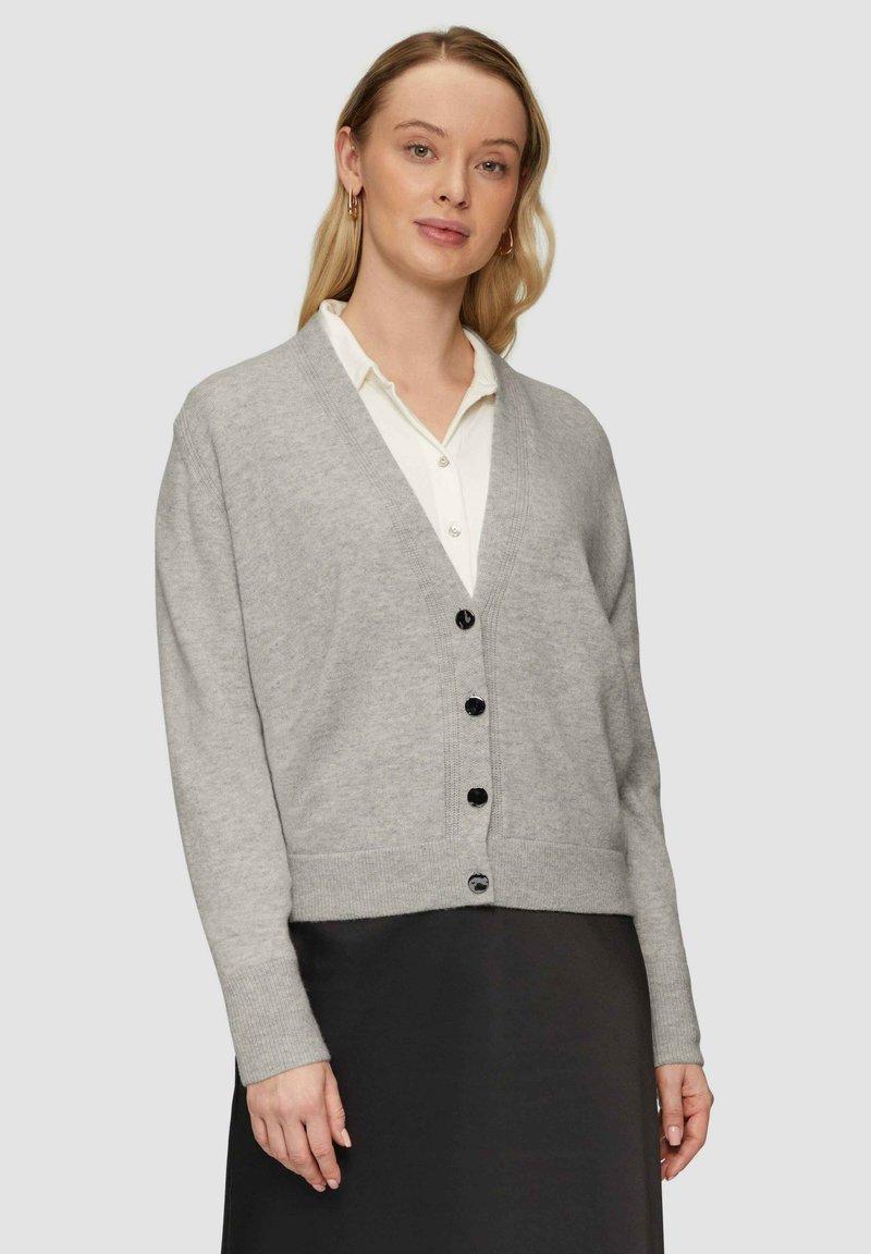 Hellgrauer Strickcardigan mit V-Ausschnitt und schwarzen Knöpfen. Hat lange Ärmel und einen taillierten Saum und wird über einem weißen Oberhemd getragen.