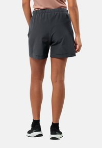Dunkelgraue Sportshorts mit elastischem Bund, ausgestattet mit Seitentaschen und einer glatten Textur, kombiniert mit schwarzen Sportschuhen.