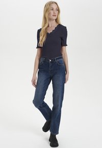 Top navy a costine con scollatura a ondas e maniche corte, abbinato a jeans in denim blu scuro a vita alta e stivaletti neri.