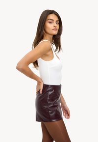 Witte aansluitende tanktop gecombineerd met een bordeauxrode neplederen minirok. De rok heeft een gladde textuur en een strakke pasvorm.