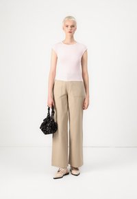 Un top roz deschis, ajustat, asortat cu pantaloni largi bej. Accesoriile includ o geantă mică neagră cu accente florale. Texturi netede și moi.