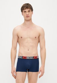Tumši zili bokseršorti ar melnu un sarkanu elastīgu jostu, kurā ir "DIESEL" logotips. Gluda auduma, pieguļošs dizains.