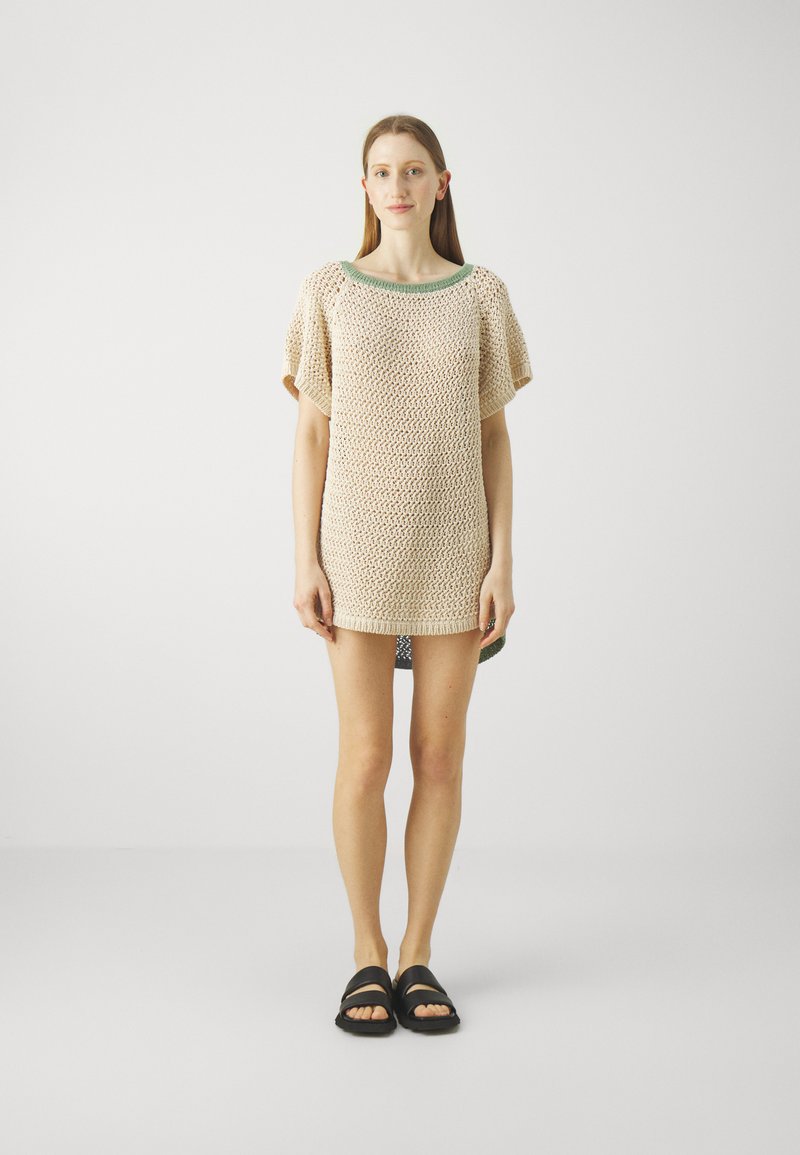 Tunique en tricot beige à coupe ample, manches courtes, encolure ronde et garniture verte contrastante au col. Design minimaliste.