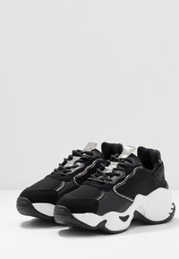 Black athletic shoes with mesh and suede material, featuring a chunky white sole, silver accents, and textured details on the sides.