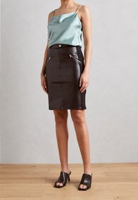 Svart läderpenningkjol med framfickor med dragkedja, kombinerad med en ljusblå satin camisole och öppna bruna klackmules.