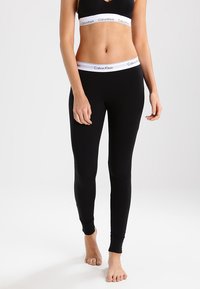 Melnas stulpa bikses ar pieguļošu dizainu un elastīgu jostasvietu, kurā ir balta Calvin Klein logo. Mīksta auduma ar gludu tekstūru.