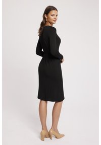 Czarna sukienka z długim rękawem, dopasowanym w talii i długości do kolan, wykonana z gładkiego materiału. W komplecie z beżowymi butami na słupku.