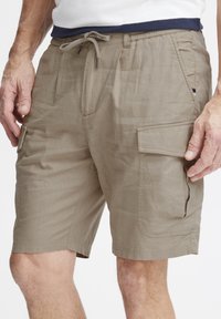 Beige cargo shorts med snor i livet, sidelommer og knelång design. Stoffet virker lett med en teksturert finish.