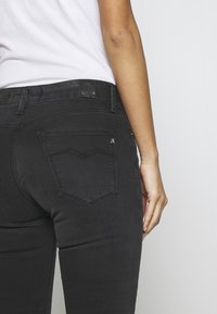Jeans de mezclilla negra con un diseño ajustado, que presentan un clásico estilo de cinco bolsillos y detalles de costura sutiles en los bolsillos traseros.