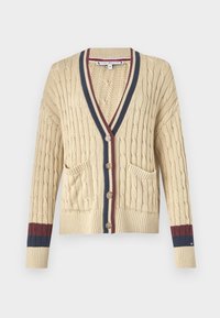 Cardigan tricoté beige avec col en V, poches avant et poignets côtelés aux rayures bleu foncé et bordeaux. Cinq boutons sur le devant.