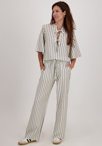 Gestreepte twee-delige outfit met een losse top met korte mouwen en een strikdetail, en wijde broekspijpen. De kleuren omvatten crème, marineblauw en lichtgrijs.