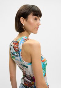 Χρωματιστό, ριχτό μπλουζάκι με ραβδώσεις που διαθέτει ένα μείγμα γραφικών σχεδίων σε μπλε, κόκκινες και πράσινες αποχρώσεις; με στρογγυλή λαιμόκοψη και στυλ racerback.