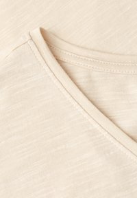 Gros plan sur un tissu en coton beige à col en V avec une fine texture côtelée et des coutures visibles le long de la couture de l'encolure.
