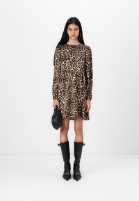 Φόρεμα με λεοπάρ σχέδιο, μακριά μανίκια και ραντεβού στη μέση. Το μοντέλο κρατά μια μαύρη τσάντα, φορώντας μαύρες μπότες μέχρι το γόνατο με στραμμένες μύτες και λεπτομέρειες.