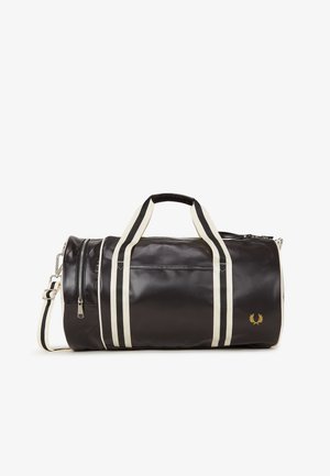 Black cylindrical duffel bag with cream and black striped handles, front zipper pocket, and small gold laurel logo on the bottom right.