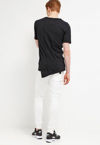 Černé tričko s krátkým rukávem s jedinečným detailem švu na zadní straně, kombinované s bílými slim-fit kalhotami a černými teniskami. Jednoduchý a moderní design.