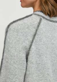Pulover gri deschis cu un tricot texturat și cusături gri închis pe marginile umerilor. Material moale și călduros, cu un croi relaxat.